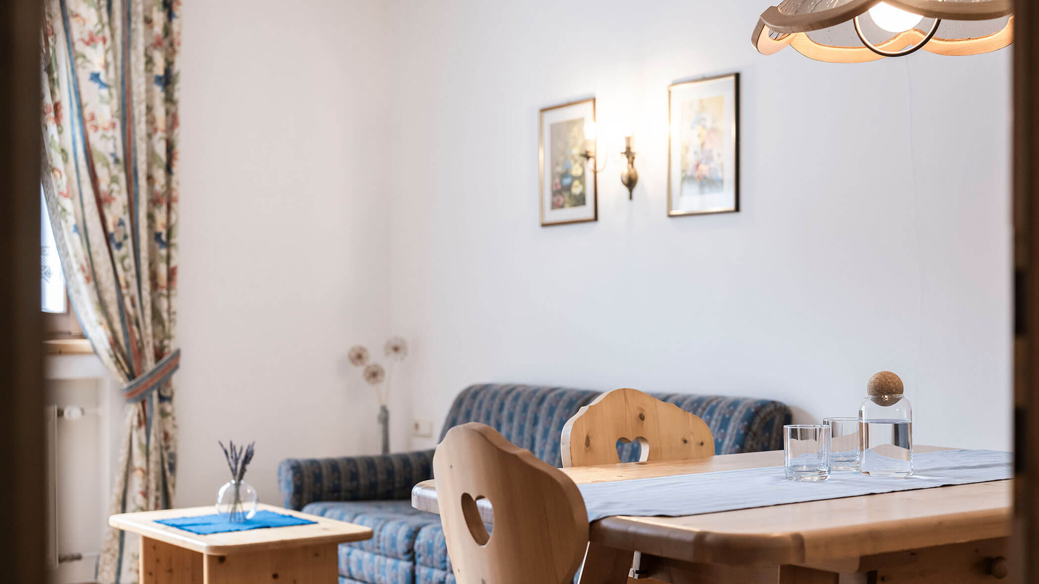 Soggiorno con divano blu e tavolo con due sedie in legno nell'appartamento 3 - Residence Kurze Wand