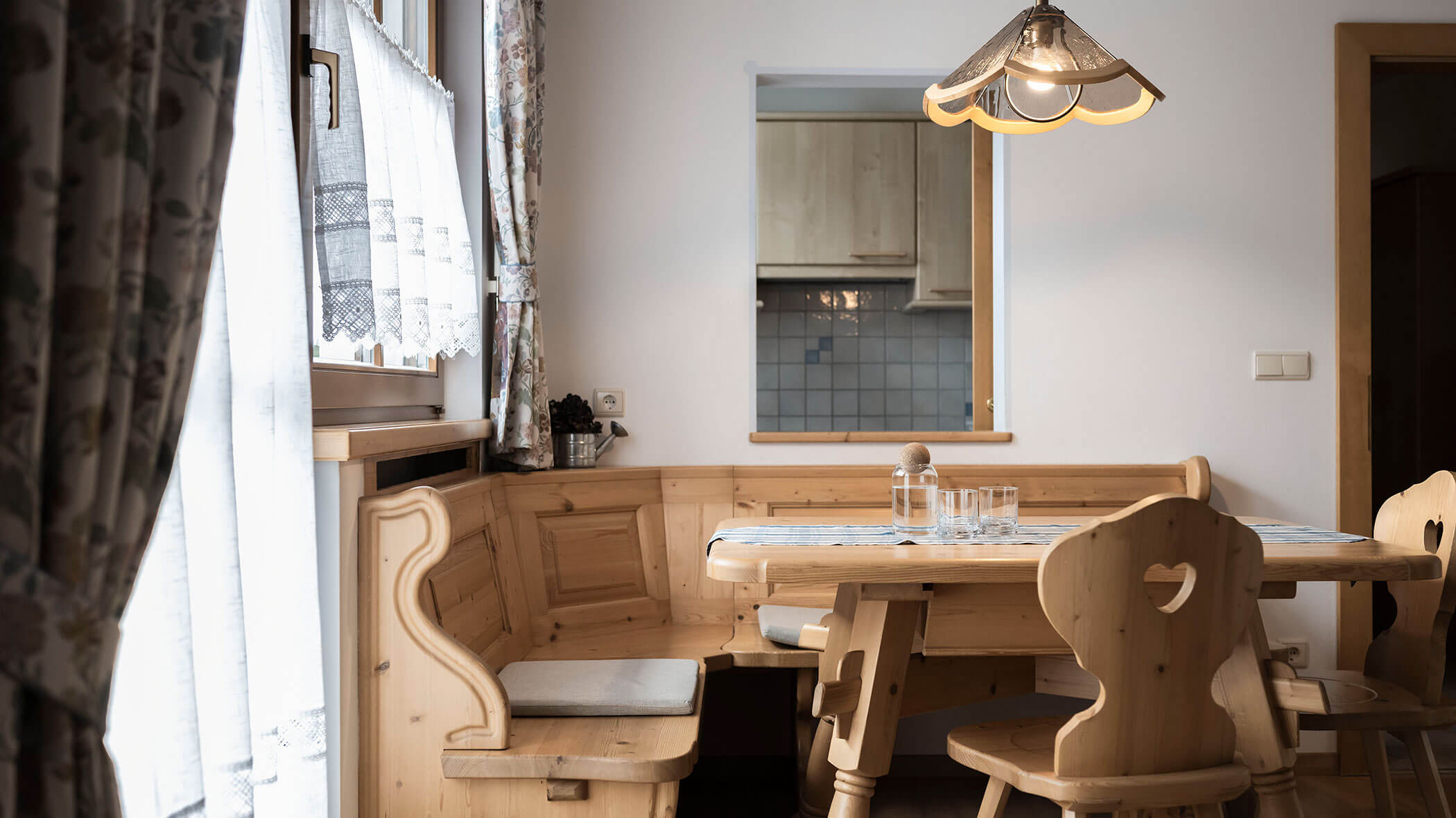 Panca angolare in legno e porta del balcone con tende a fantasia nell'appartamento 4 - Residence Kurze Wand