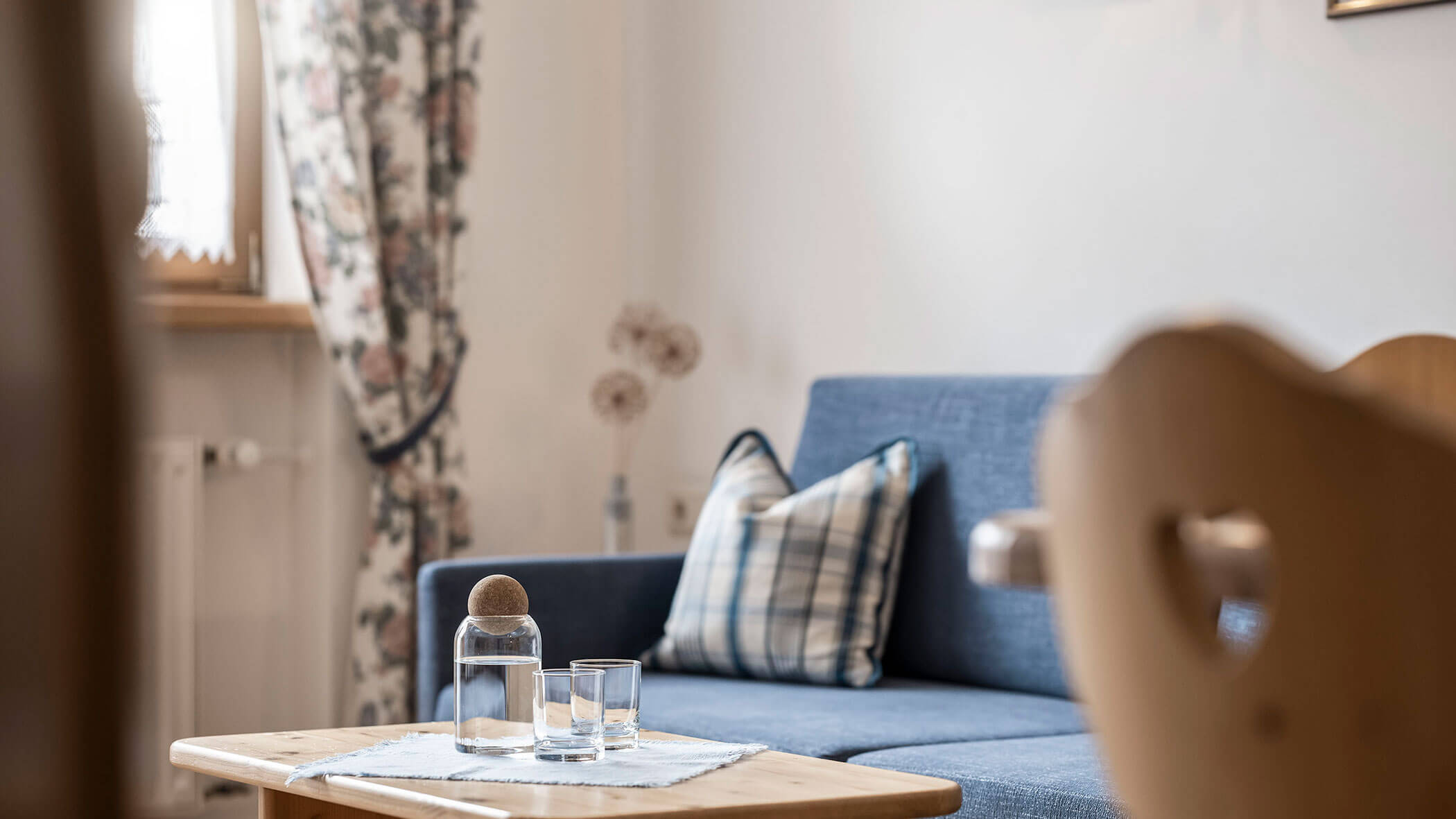 Zona giorno con divano blu e tavolo con due sedie in legno nell'appartamento 5 - Residence Kurze Wand